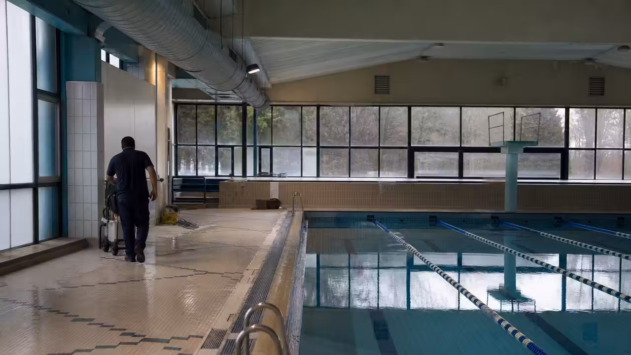 Bassin municipal couvert vide, lignes d'eau et baies vitrées dans un centre aquatique vieillissant
