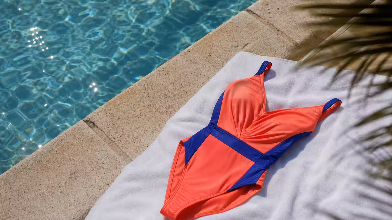 Maillot une pièce noir à coupe asymétrique posé sur une margelle claire près d’une piscine méditerranéenne