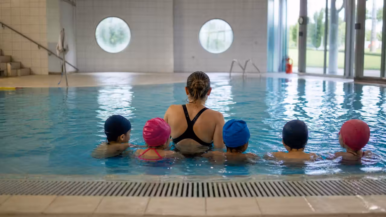 Cours de natation encadré dans un bassin couvert avec enfants équipés de bonnets de bain