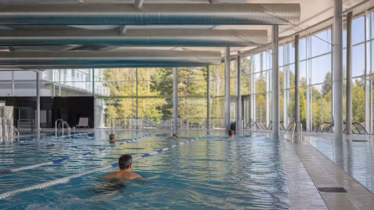 Nageurs dans une piscine couverte lumineuse avec ventilation visible au-dessus du bassin