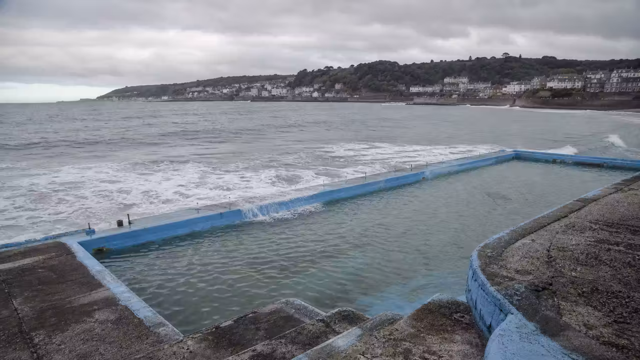 Ancien bassin extérieur en béton au bord de la mer, marqué par les embruns et les vagues