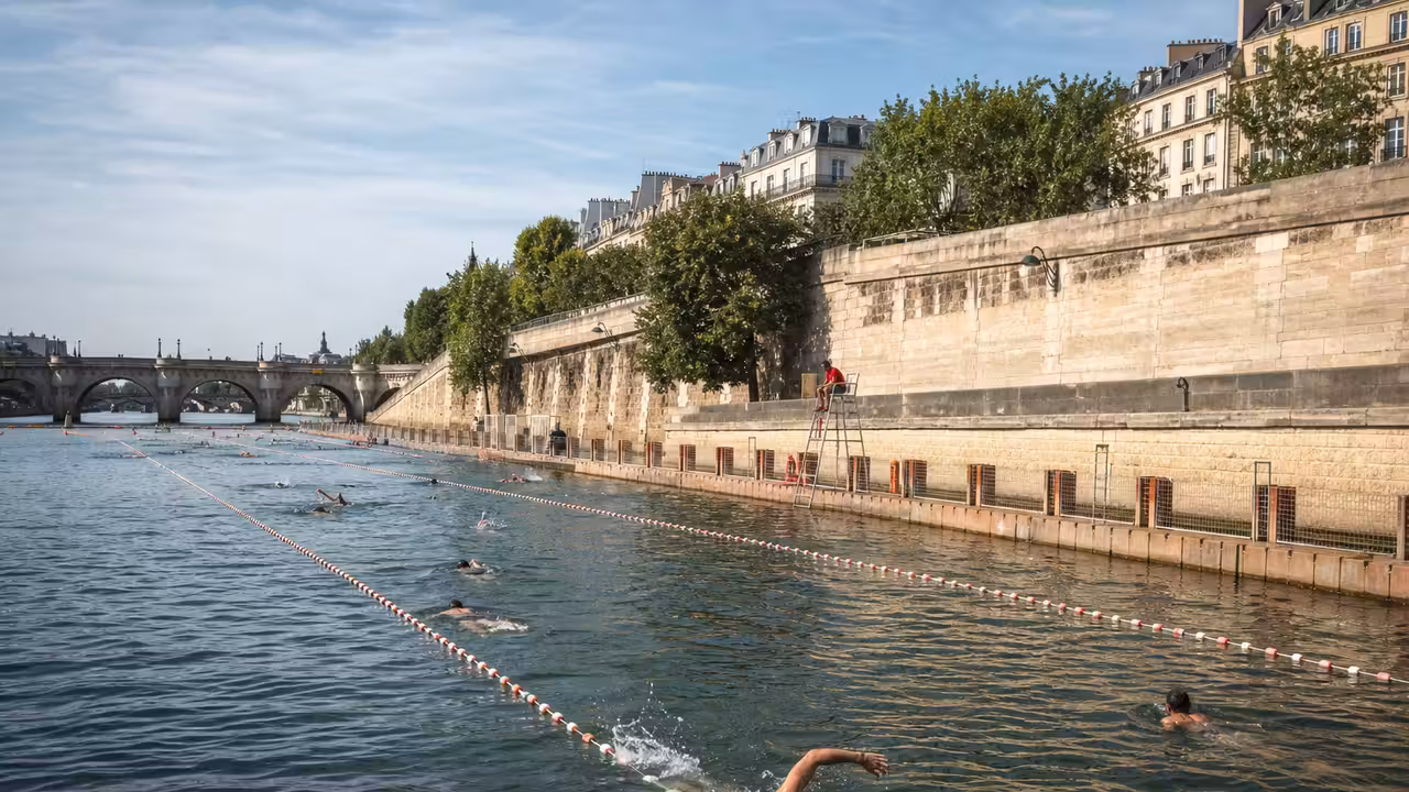Zone de baignade urbaine surveillée sur la Seine, avec nageurs et quais parisiens en arrière-plan