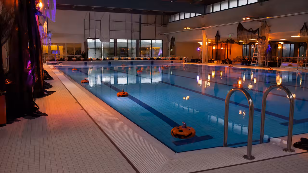 Bassin municipal décoré pour Halloween, éclairé en bleu et orange avant une soirée aquatique festive
