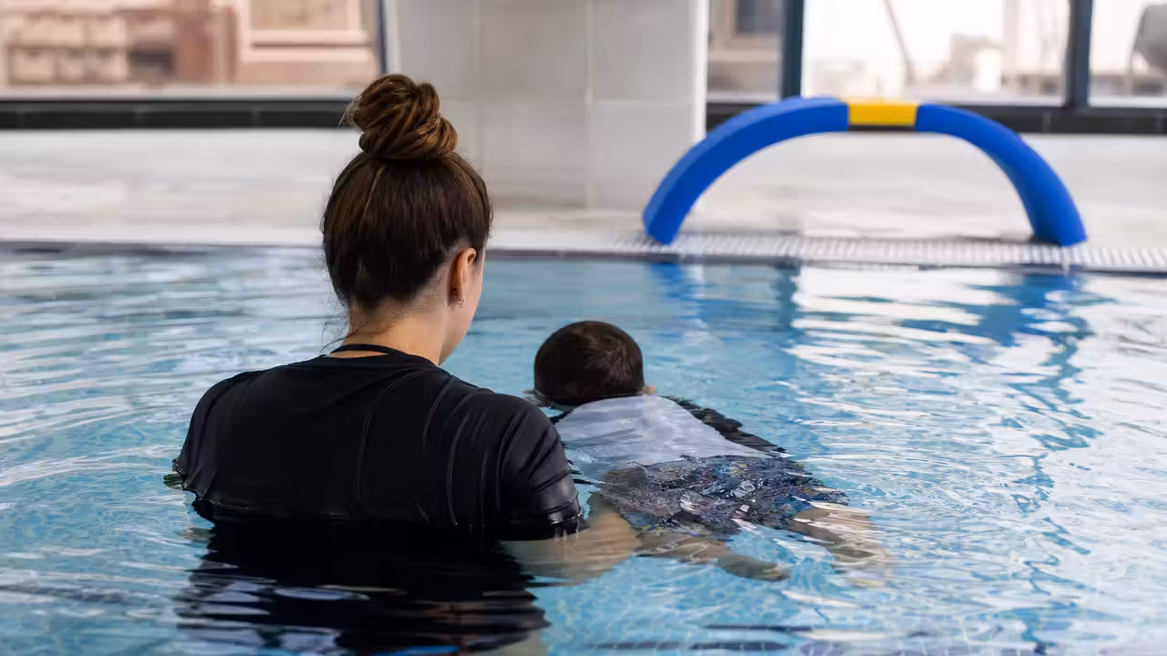 Jeune enfant encadré dans un bassin pendant un exercice d’immersion et de déplacement sans brassards