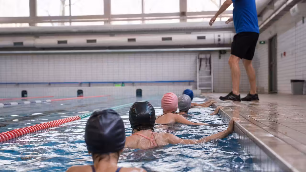 Enfants vus de dos pendant une leçon de natation encadrée dans un bassin couvert municipal
