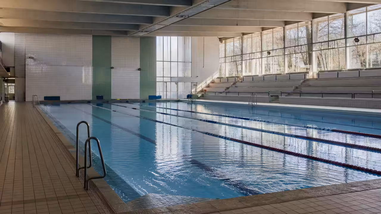 Bassin couvert d’une piscine municipale française, lignes d’eau libres et gradins visibles en arrière-plan