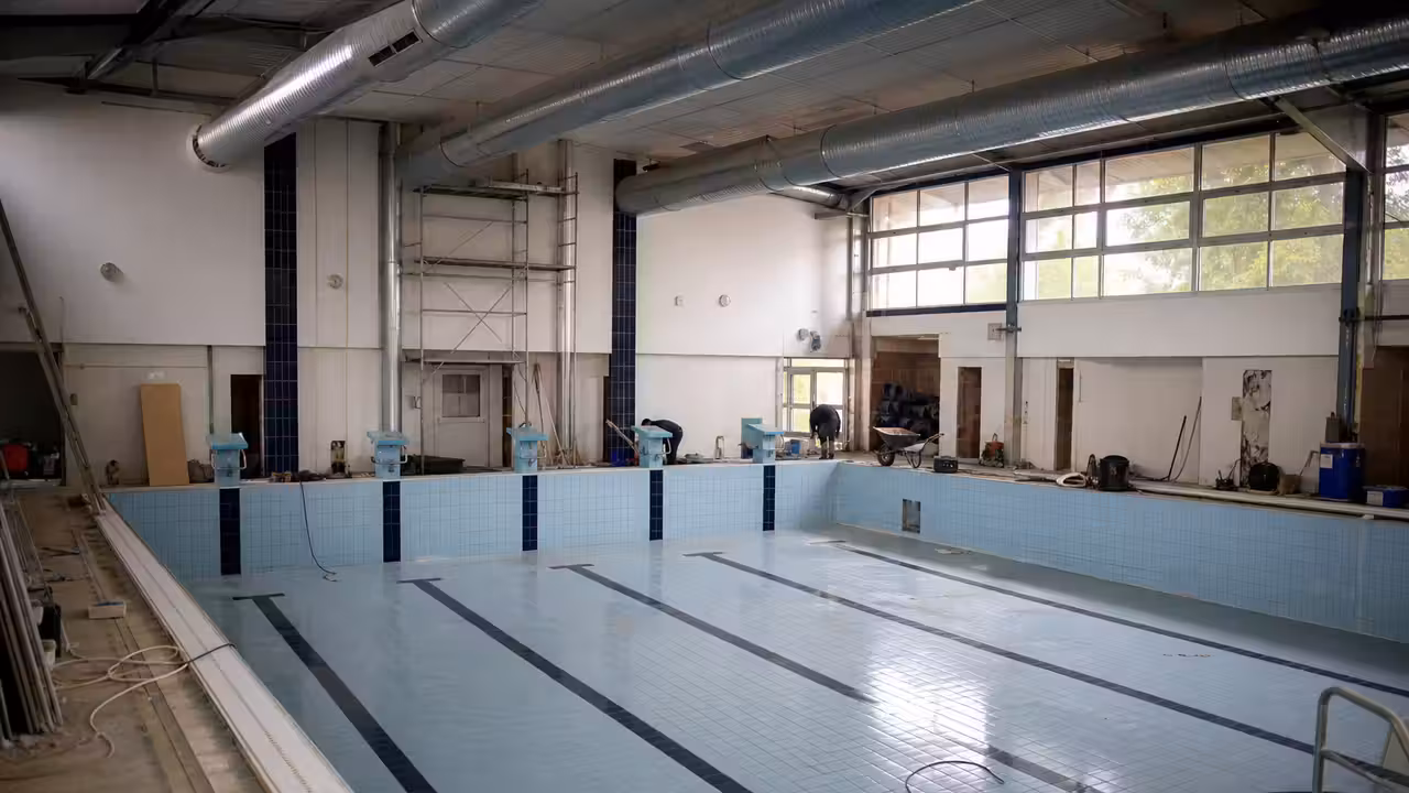 Bassin municipal couvert vide pendant des travaux de rénovation, avec plages carrelées et équipements techniques