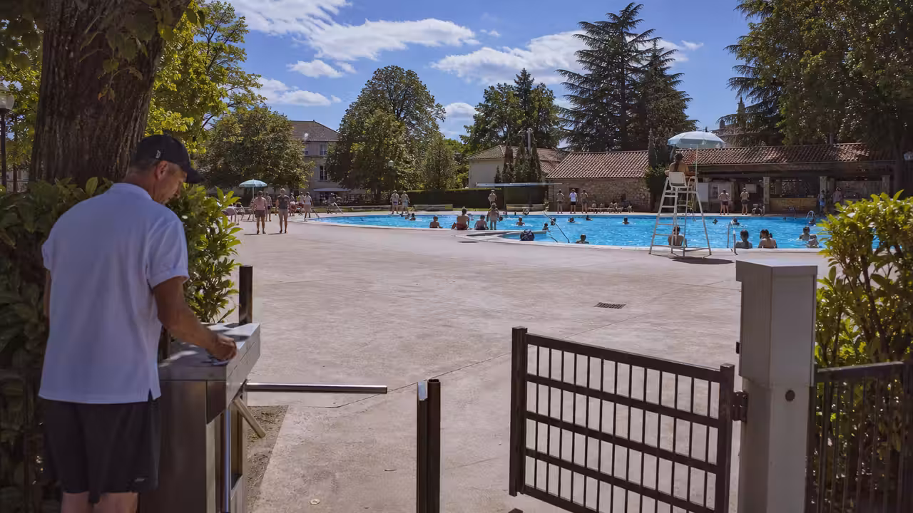 Entrée d’une piscine publique de plein air avec portiques et bassins fréquentés en arrière-plan