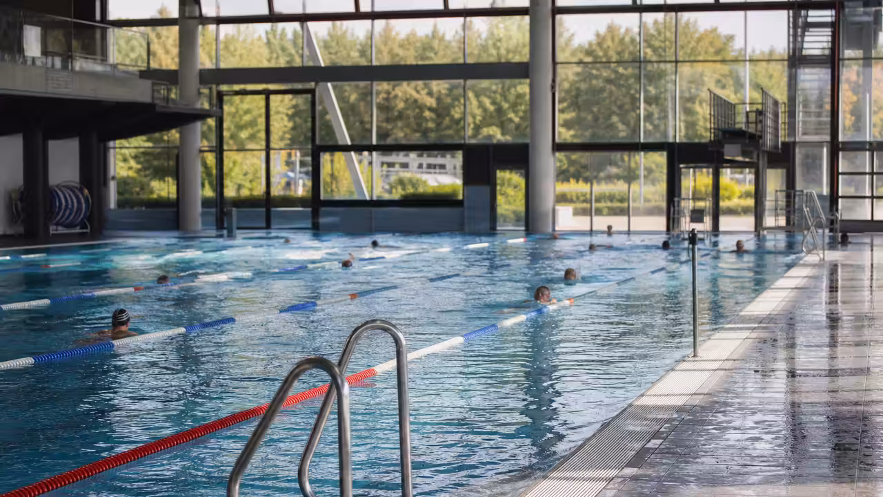 Bassin intérieur d’un centre aquatique municipal avec lignes de nage et baigneurs vus de loin