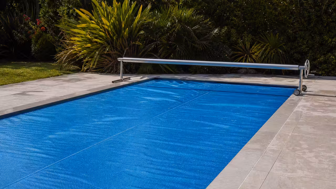Bâche à bulles bleue posée sur une piscine rectangulaire, avec enrouleur sur la terrasse