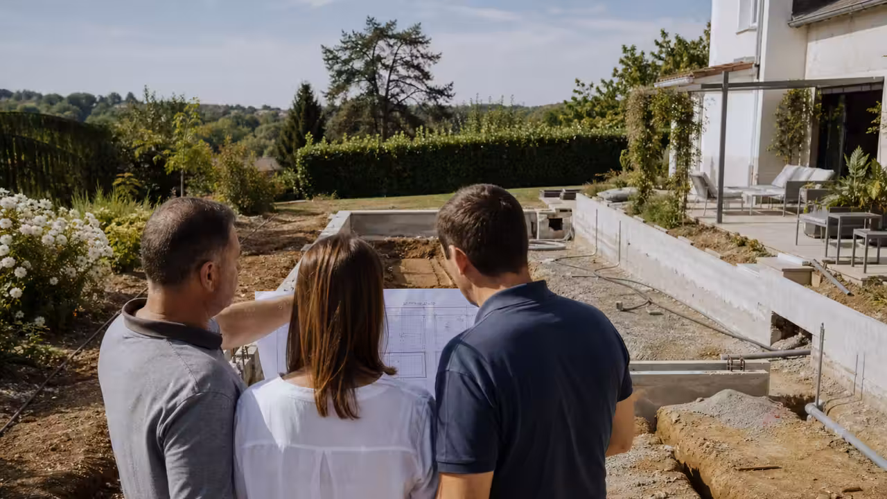 Un couple examine un devis de piscine avec un professionnel près d’un bassin en construction