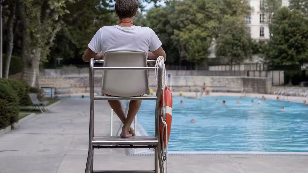 Surveillant de baignade observant un bassin extérieur depuis son poste pendant une journée d’été