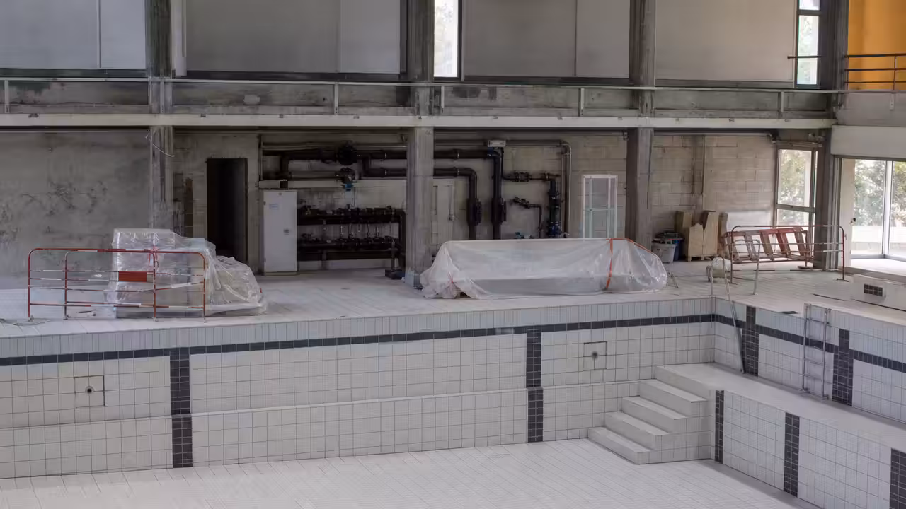 Chantier de rénovation d'une piscine publique avec bassin vide, réseaux techniques et ouvriers au travail
