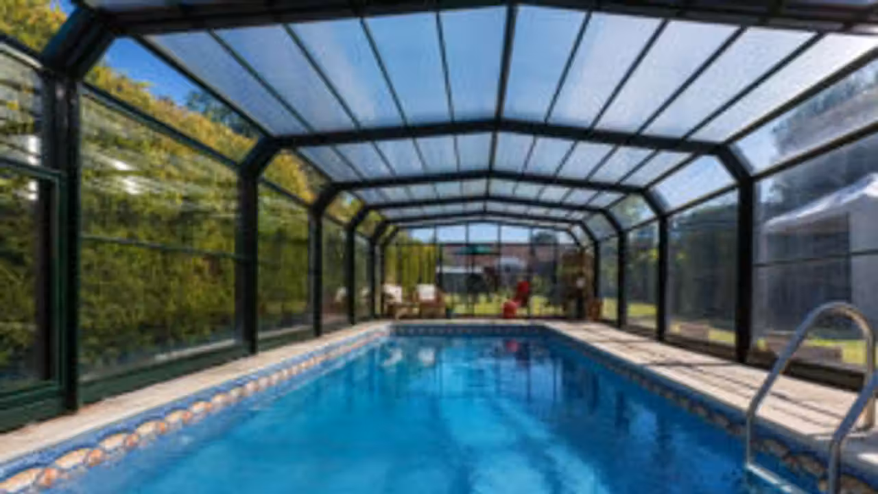 Abri haut télescopique fermé au-dessus d’une piscine familiale, avec terrasse et jardin arboré en arrière-plan