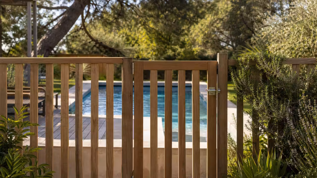 Barrière de piscine en bois clair avec portillon fermé autour d’un bassin dans un jardin paysager