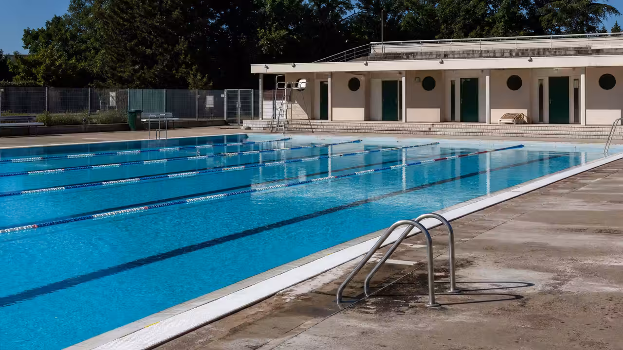 Bassin extérieur municipal vide en été, avec lignes d’eau et équipements de surveillance au bord