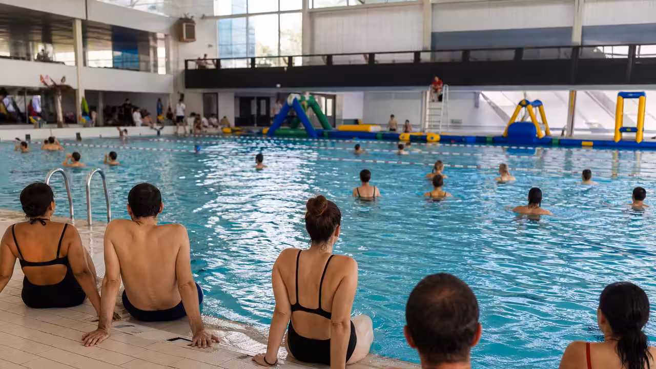 Bassin couvert d’une piscine publique avec lignes d’eau, adultes au bord et structure gonflable au loin