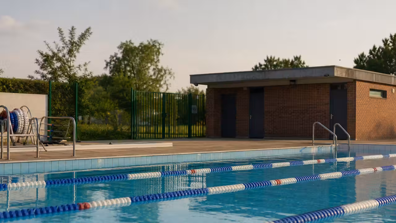 Bassin extérieur d’une piscine municipale vide, avec lignes d’eau et locaux techniques en arrière-plan