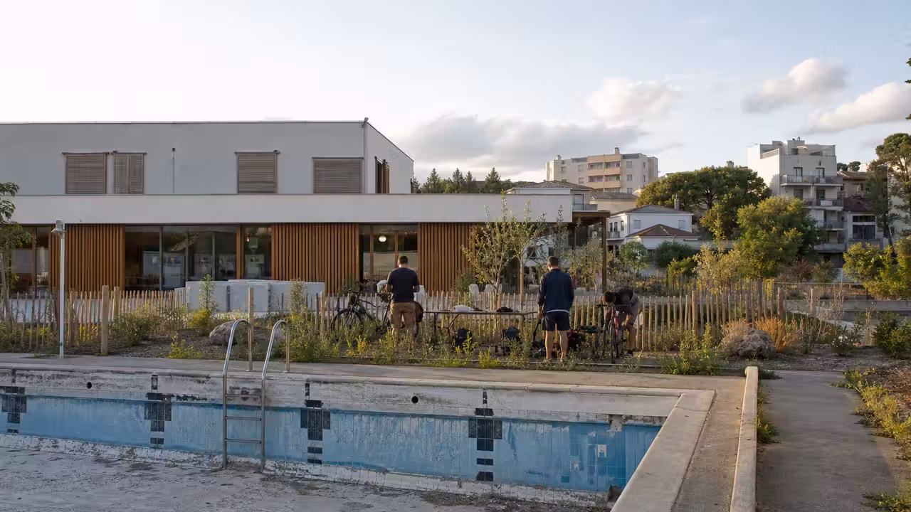 Ancienne piscine extérieure reconvertie en espace végétalisé avec bâtiment public rénové et atelier vélo