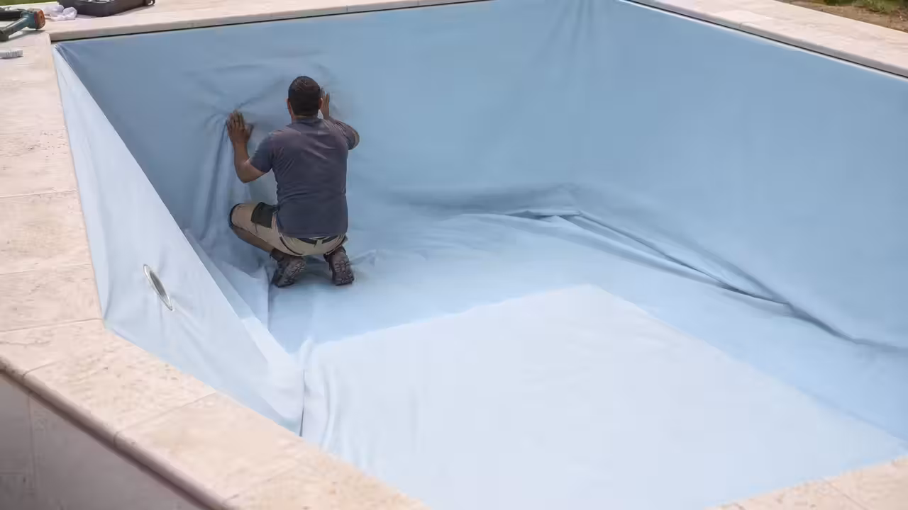 Pose d’un liner bleu clair dans une piscine rectangulaire vide, avec margelles en pierre claire