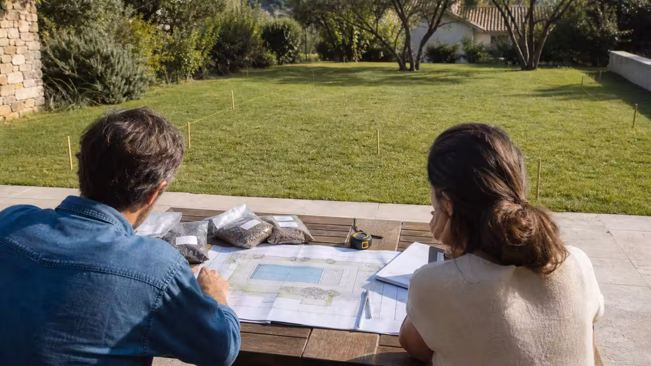 Couple examinant les plans et les dimensions d’un futur bassin dans un jardin avant travaux