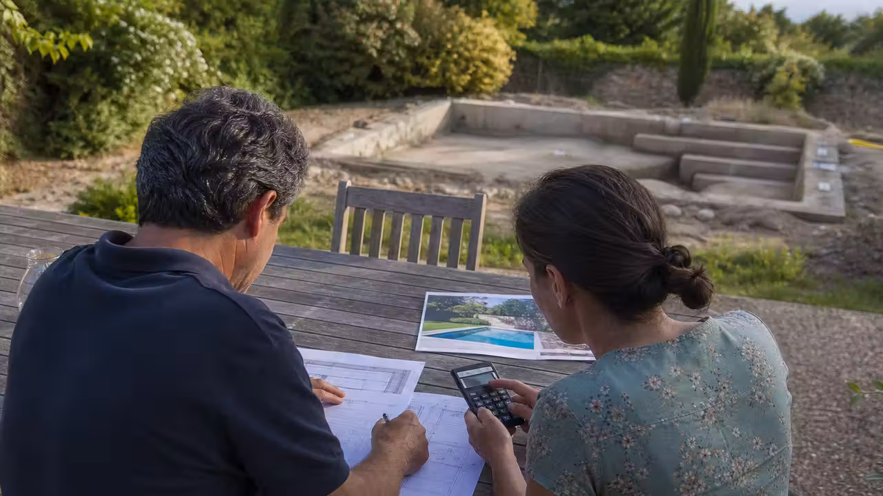 Propriétaires comparant un devis de piscine et un plan de financement sur une table de jardin