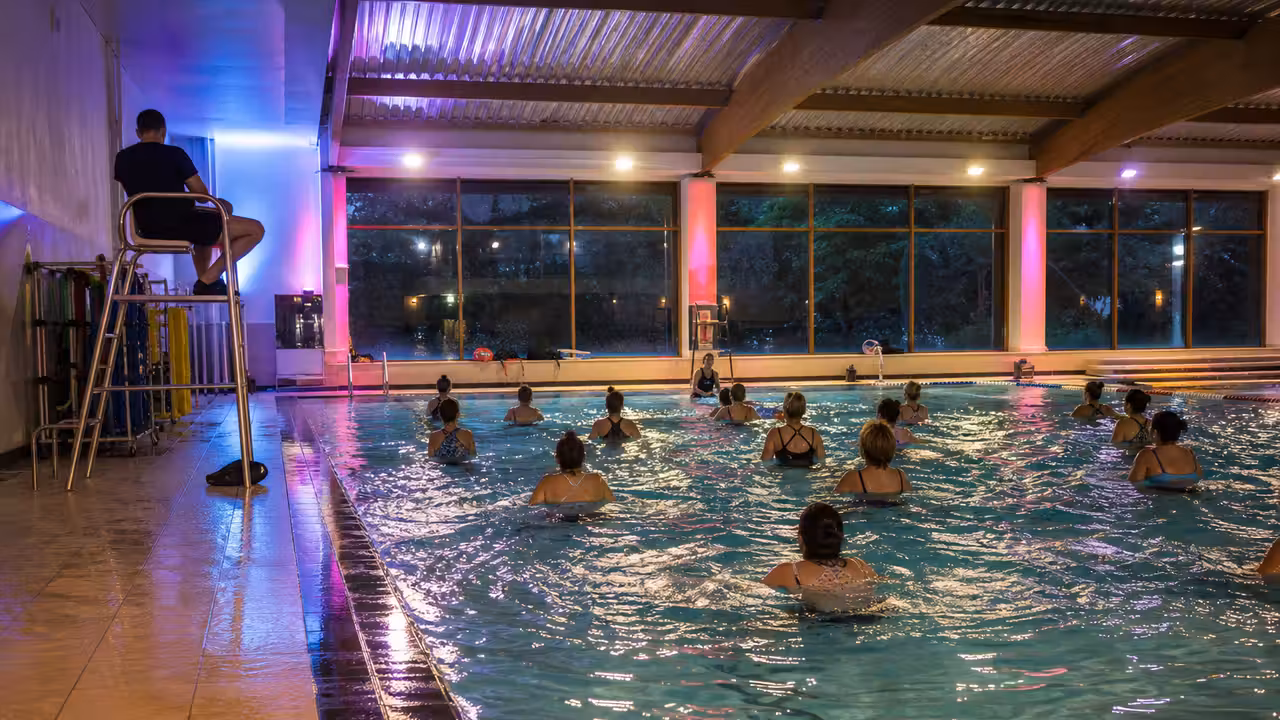Séance d’aquagym collective encadrée dans un bassin couvert éclairé pour une soirée aquatique