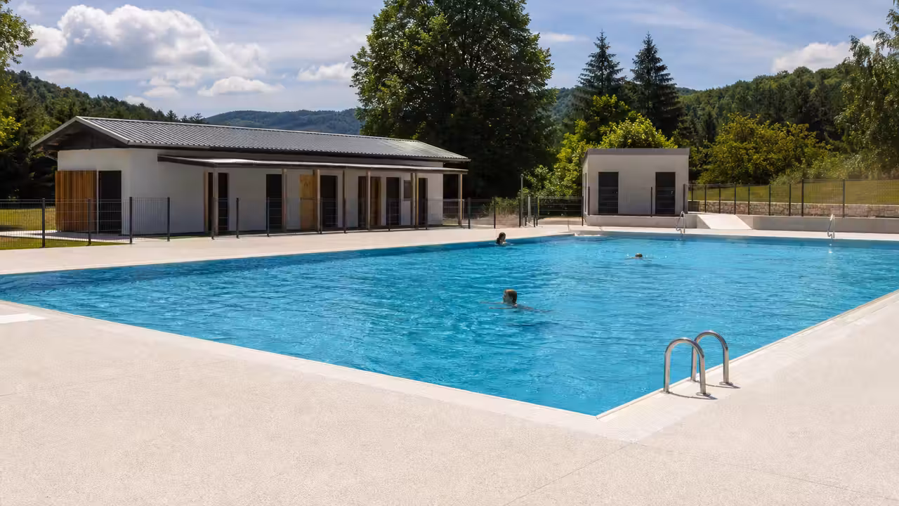 Piscine municipale rénovée avec bassin extérieur, plages claires et équipements techniques discrets à l’arrière-plan
