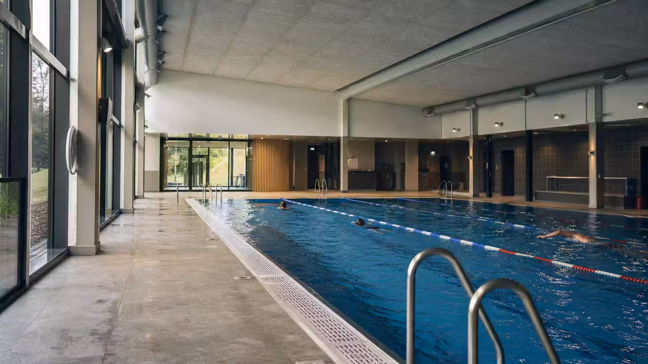 Hall lumineux d’une piscine municipale rénovée avec bassin, lignes d’eau, baies vitrées et équipements techniques