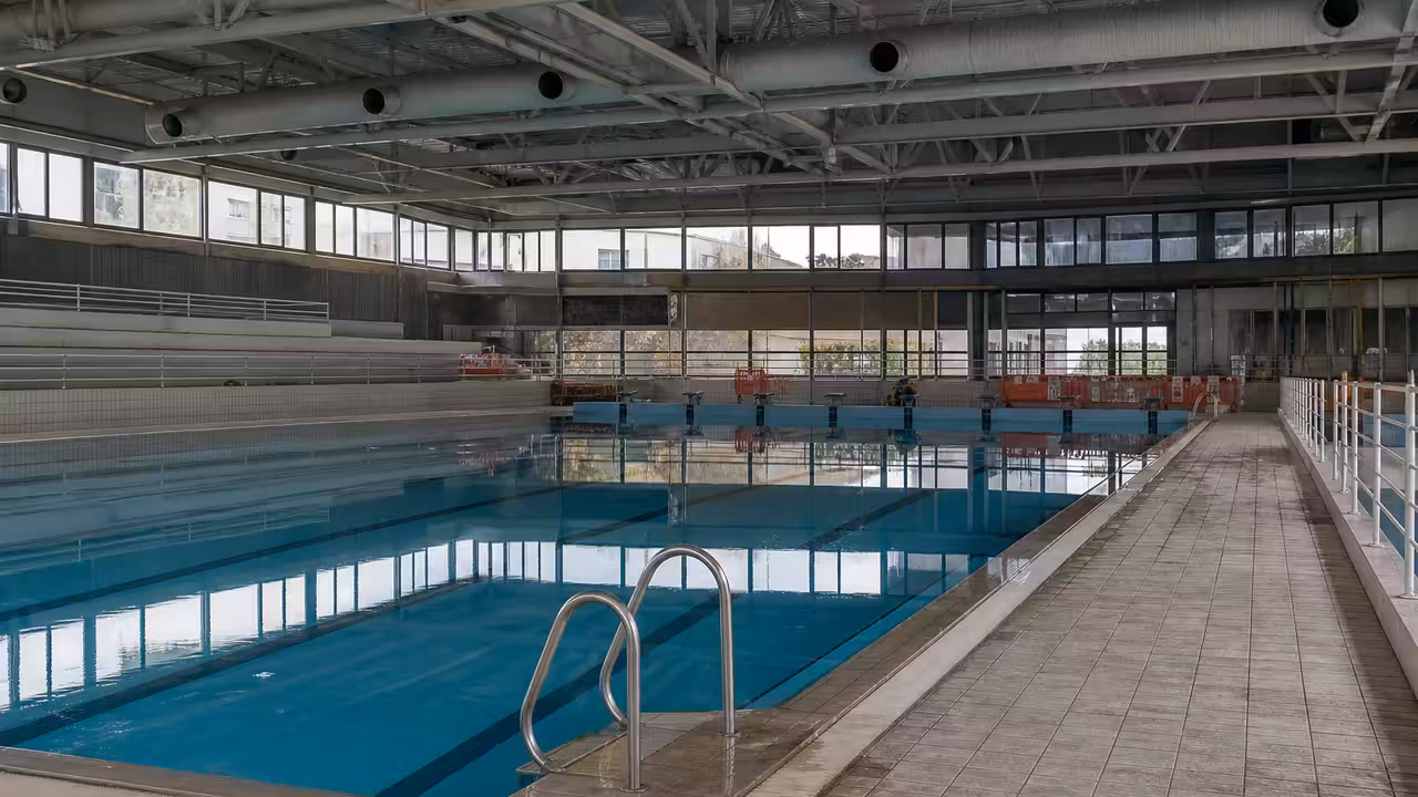 Vue intérieure d’une piscine municipale couverte avec bassin de nage, charpente et couloirs inoccupés