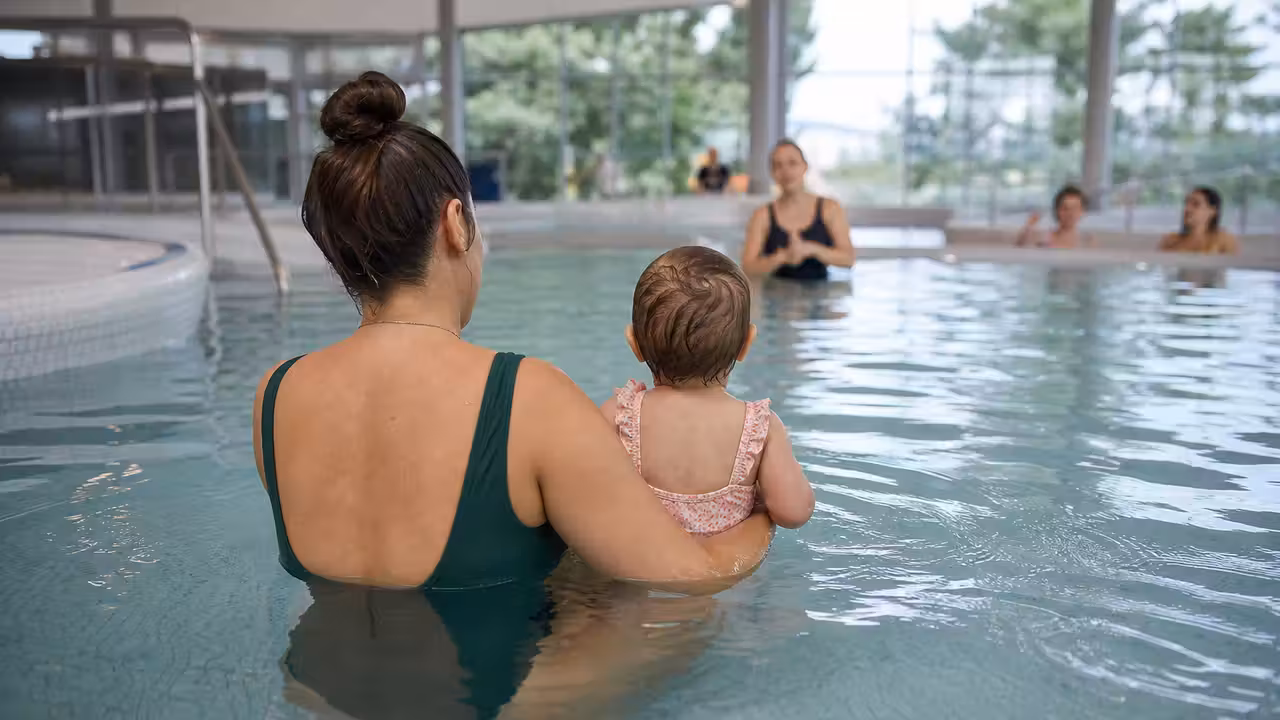 Parent accompagnant un très jeune enfant dans un bassin intérieur lors d’une séance d’éveil aquatique