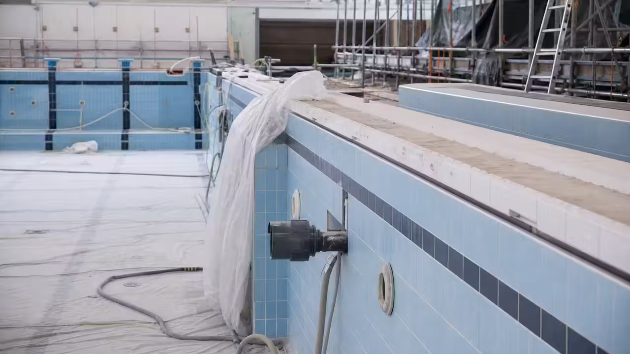 Bassin intérieur d’une piscine publique en rénovation, avec échafaudages et techniciens au bord de l’eau