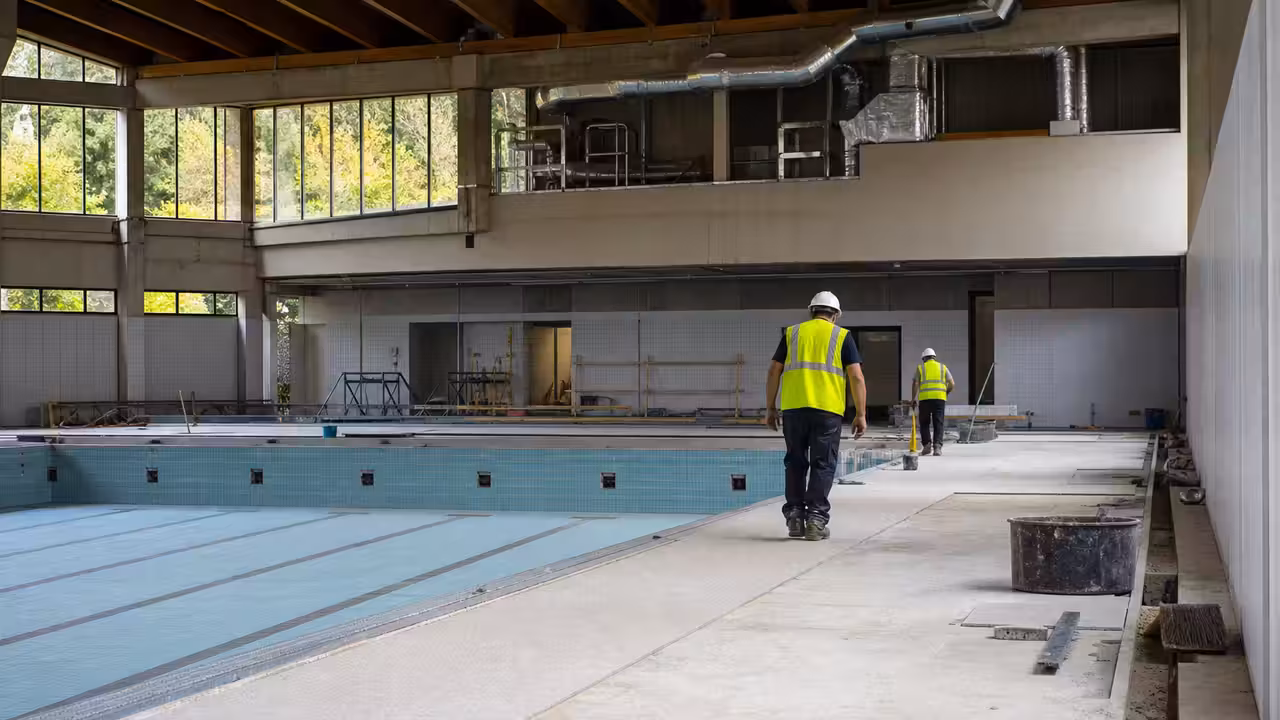 Chantier de rénovation d’une piscine municipale avec bassin vide, plages en travaux et équipements techniques