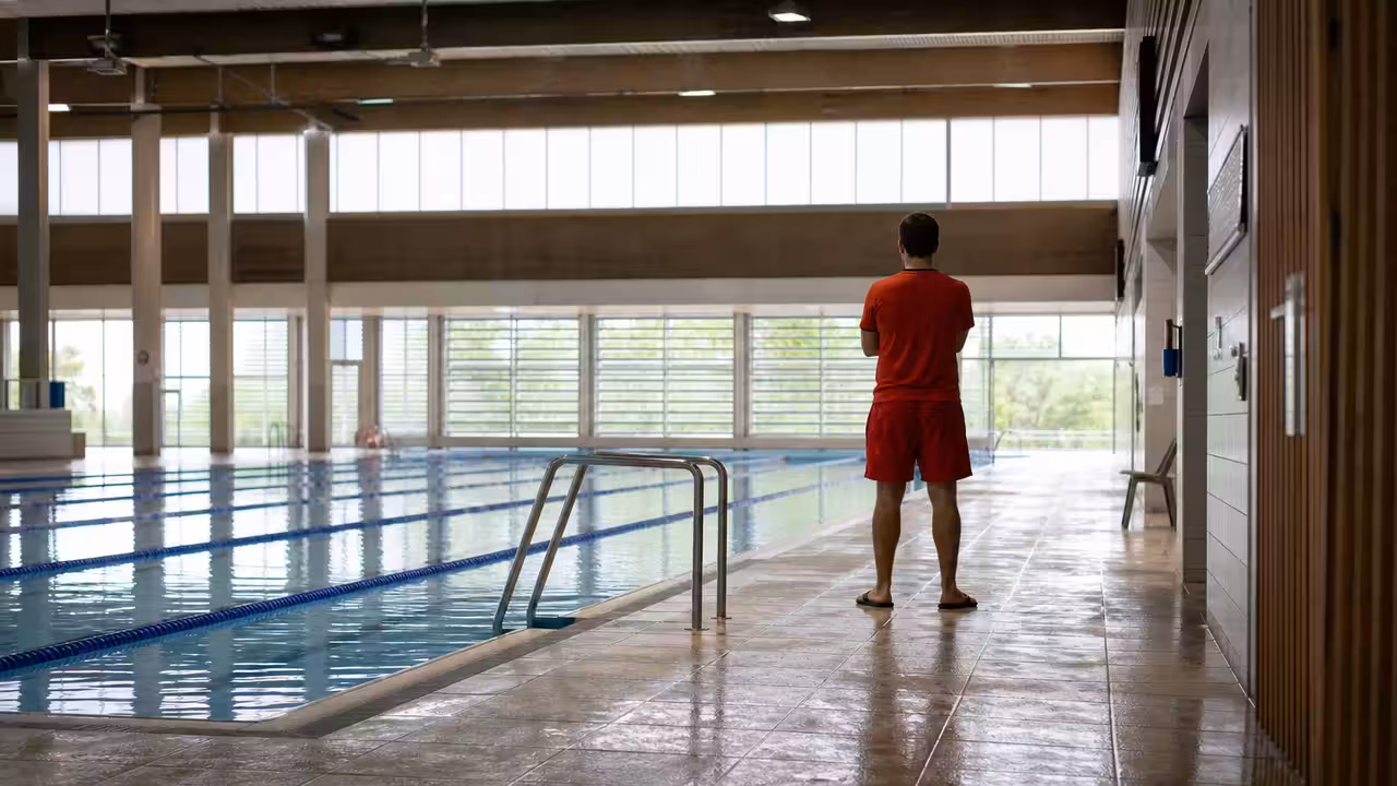 Bassin couvert d’une piscine publique avec lignes d’eau, gradins et surveillant au bord de l’eau
