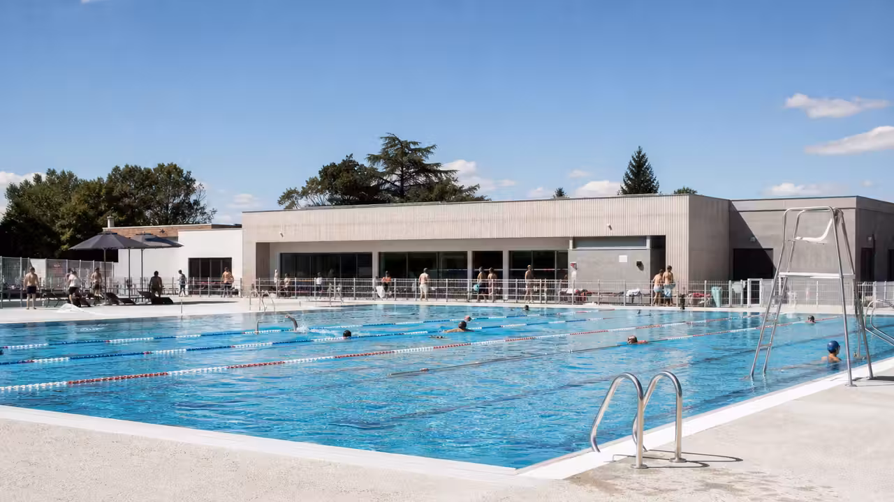 Bassin municipal rénové de 25 mètres avec lignes d’eau, plages claires et vestiaires modernes en arrière-plan