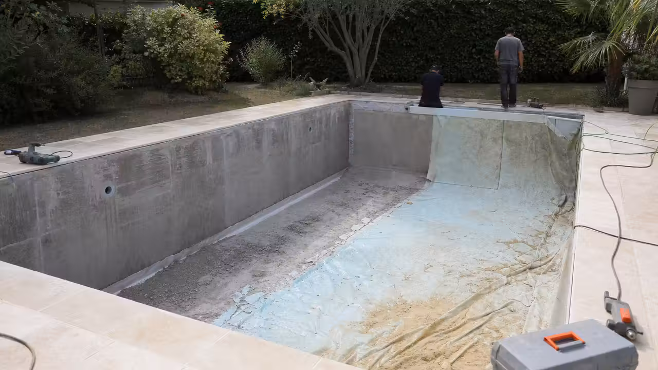 Bassin en cours de rénovation avec revêtement retiré, outils de chantier et margelles en pierre claire