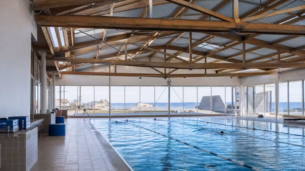Bassin intérieur d’une piscine municipale rénovée, avec charpente claire et grandes baies vitrées