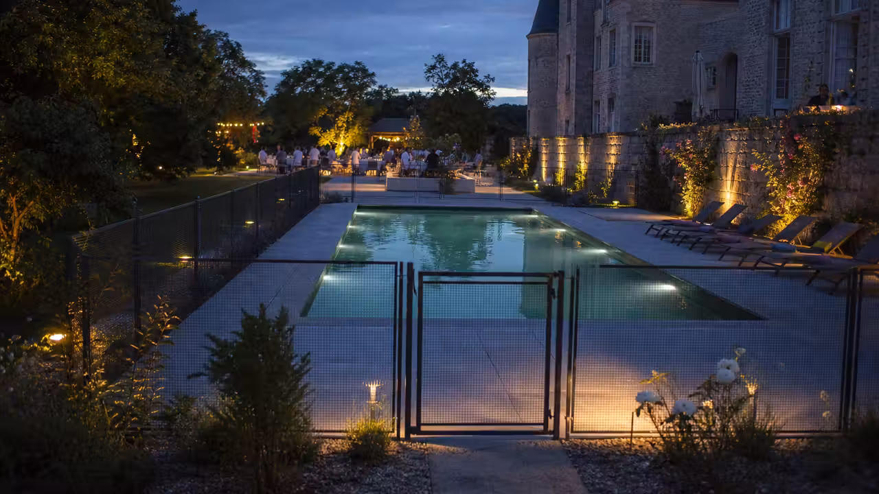 Piscine éclairée et sécurisée dans les jardins d’un château pendant une soirée en plein air