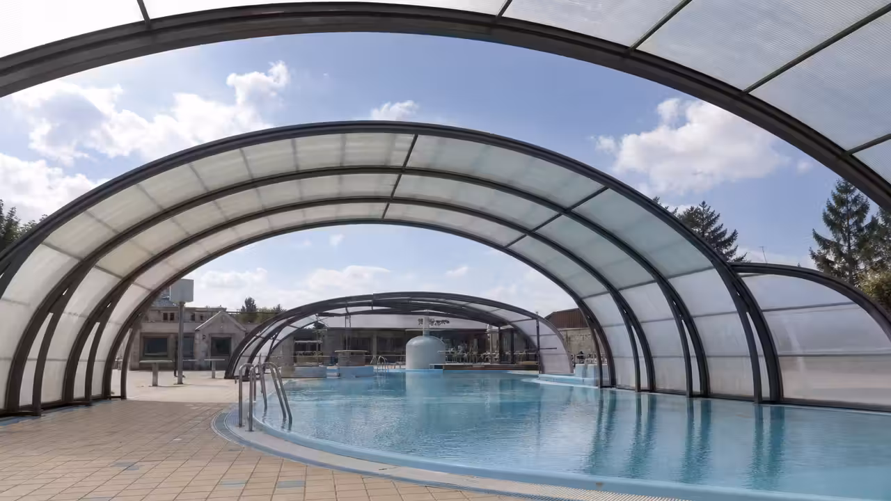 Coupole circulaire ouverte d’une piscine publique rénovée, avec bassin calme et structure métallique apparente