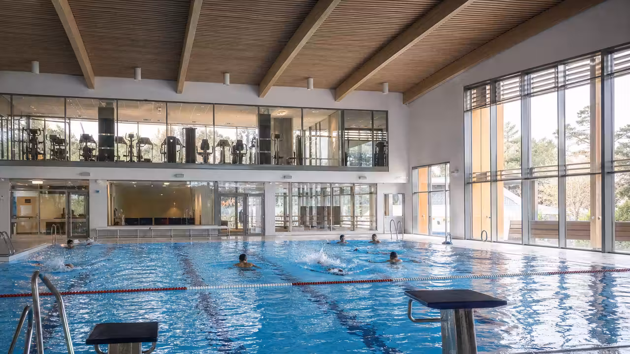 Bassin intérieur lumineux avec nageurs adultes et espace de remise en forme en arrière-plan