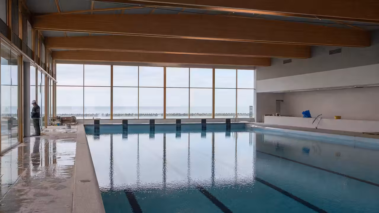 Vue intérieure d’un bassin municipal lumineux avec baies vitrées, lignes de nage et plages accessibles