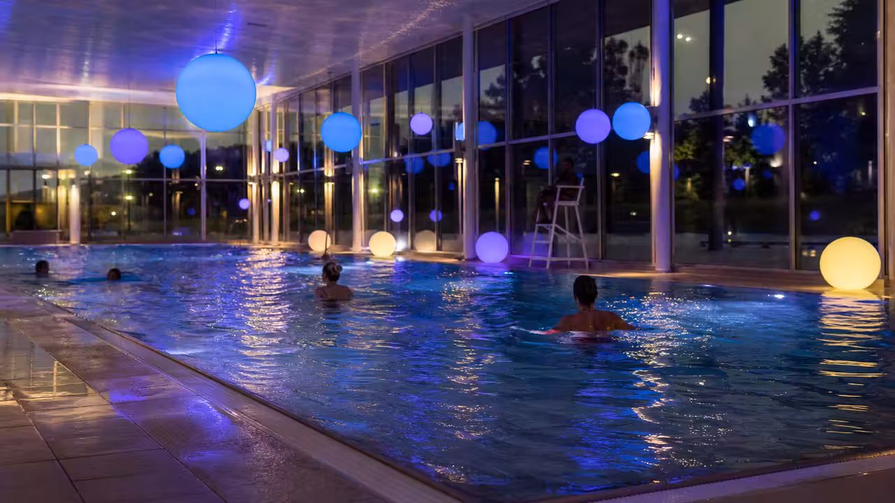 Bassin intérieur éclairé en bleu et violet lors d’une soirée nocturne dans un centre aquatique