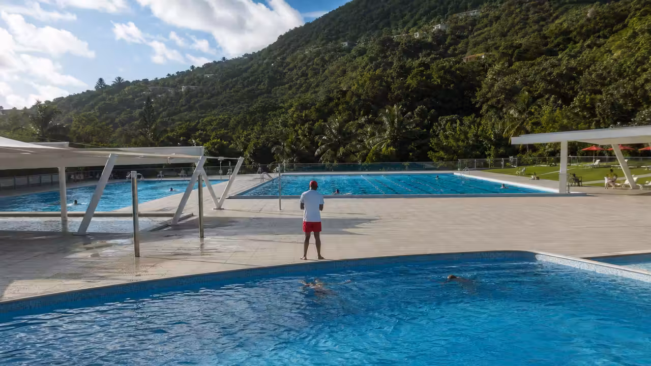 Bassins d’une piscine municipale chauffée, bordés de plages et surveillés par un maître-nageur.