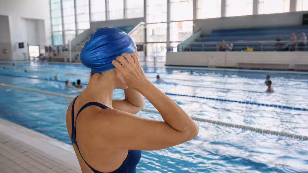 Nageuse ajustant un bonnet de bain silicone au bord d’un bassin municipal lumineux et fréquenté