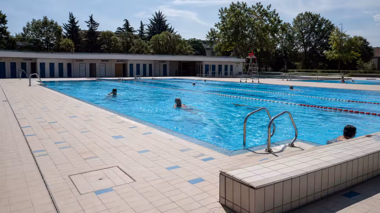 Bassin extérieur d’une piscine municipale avec lignes d’eau, plages carrelées et baigneurs au loin