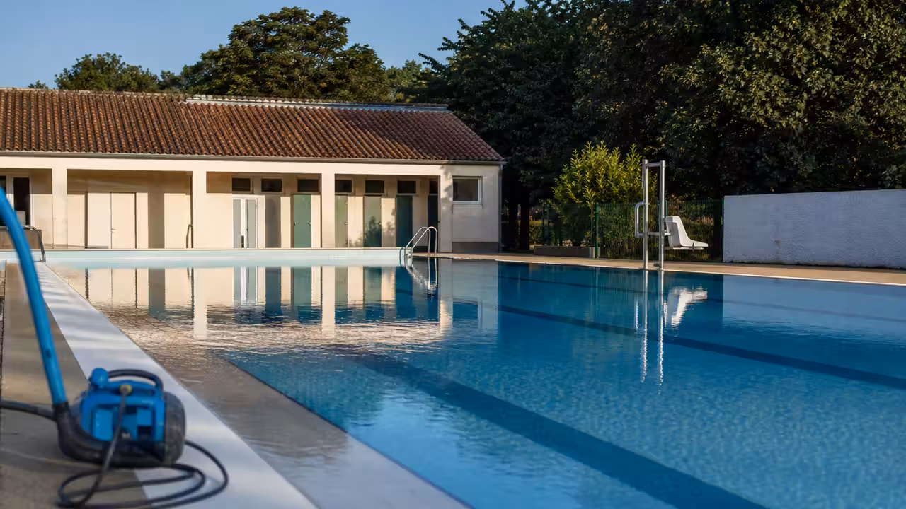 Bassin extérieur d’une piscine municipale rurale, lignes d’eau calmes et vestiaires en arrière-plan