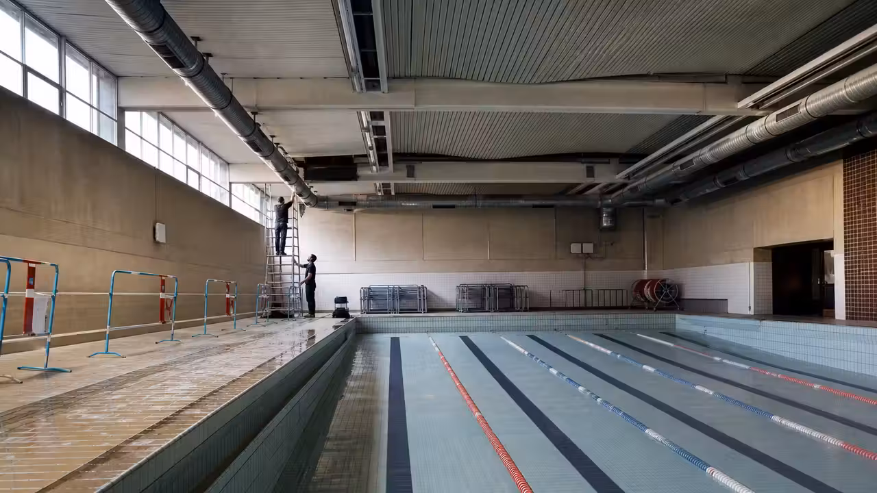 Bassin municipal couvert vide avec lignes d’eau, baies vitrées et équipements de ventilation au plafond