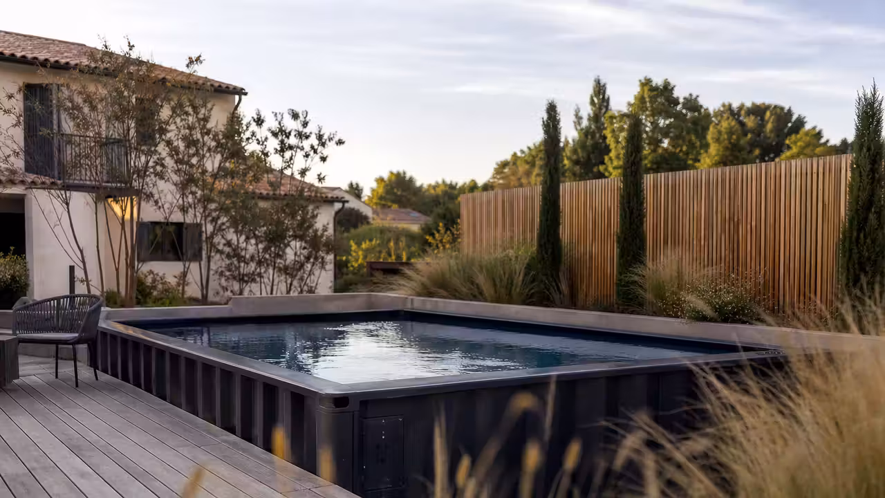 Piscine en container métallique installée dans un jardin, bordée d'une terrasse en bois et de végétaux