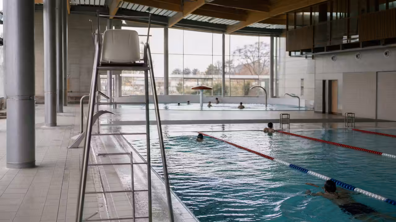 Bassin intérieur d’un centre aquatique public avec lignes de nage, baigneurs éloignés et lumière naturelle