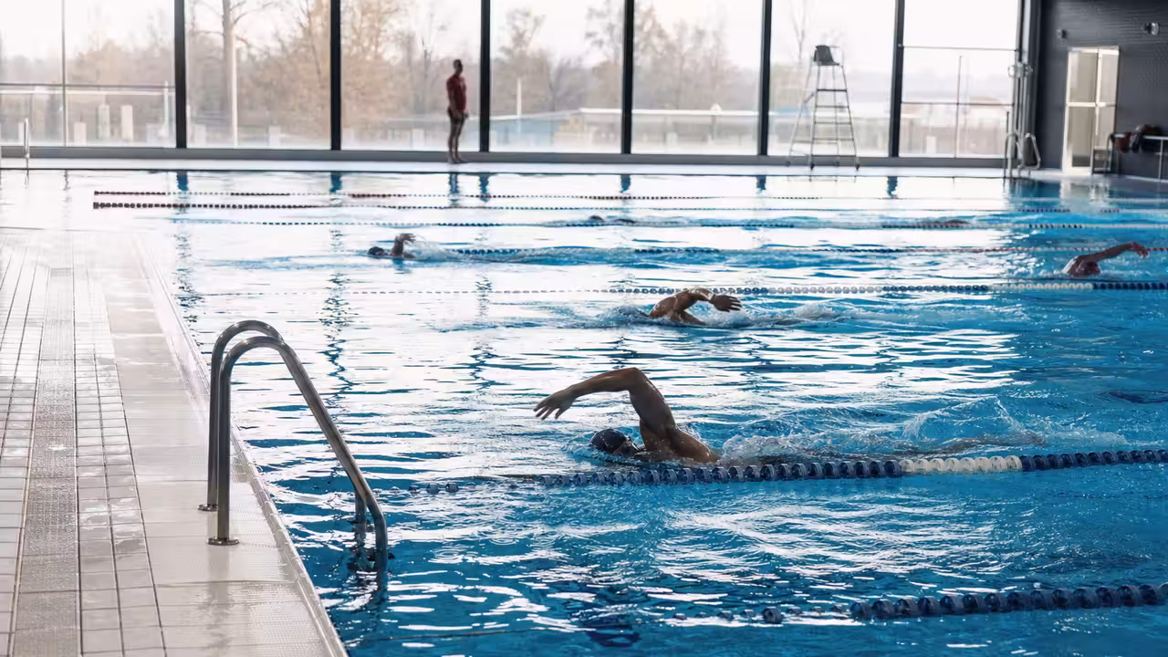 Bassin sportif couvert avec lignes d’eau et nageurs pendant un créneau matinal en piscine municipale